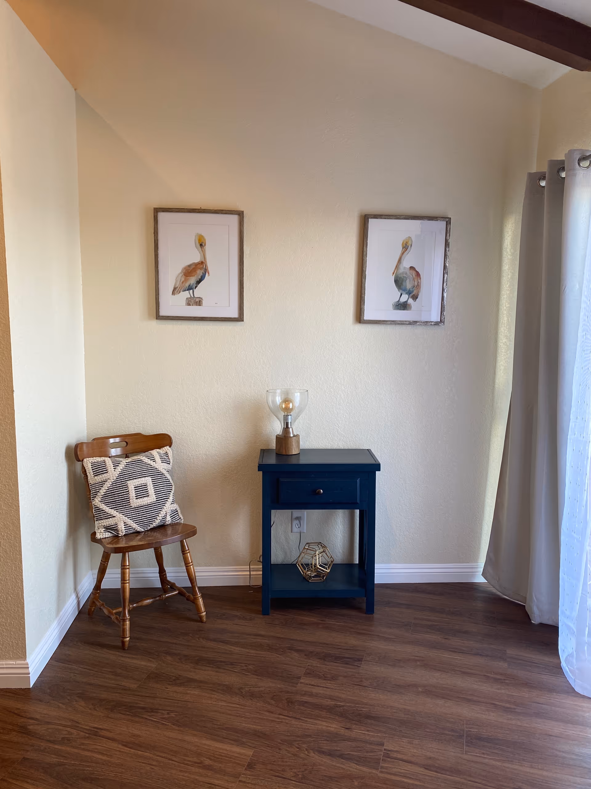 A cozy corner with a chair, small blue side table, lamp, and wall art.