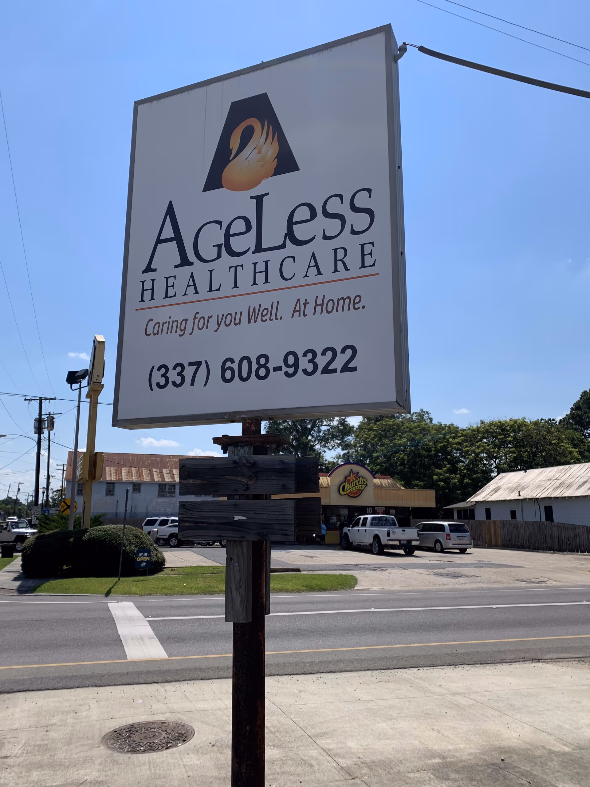 A tall Ageless Healthcare sign mounted on a wooden post beside a roadside.