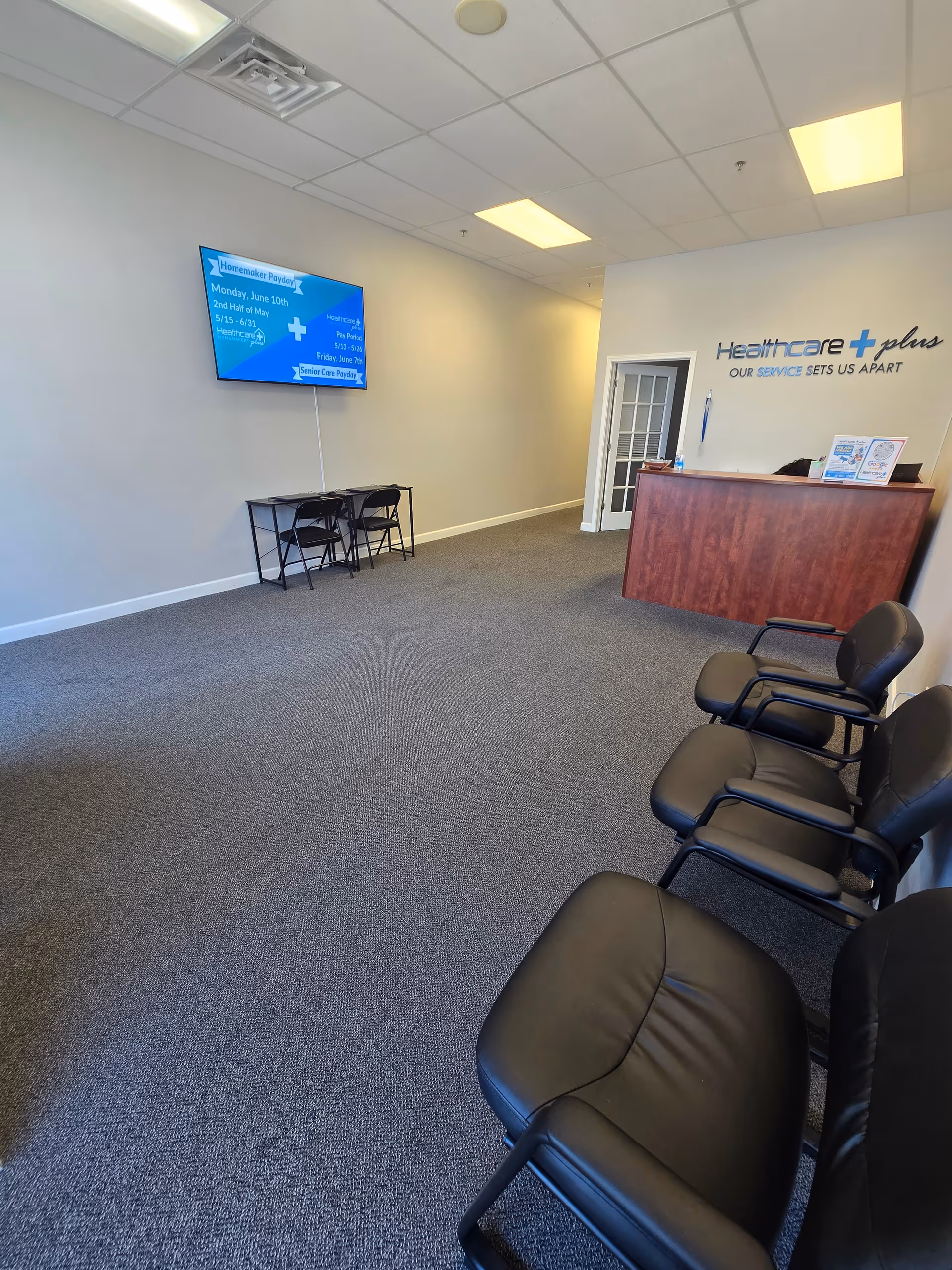 A lobby area features a wooden reception desk, black chairs, and wall signage.