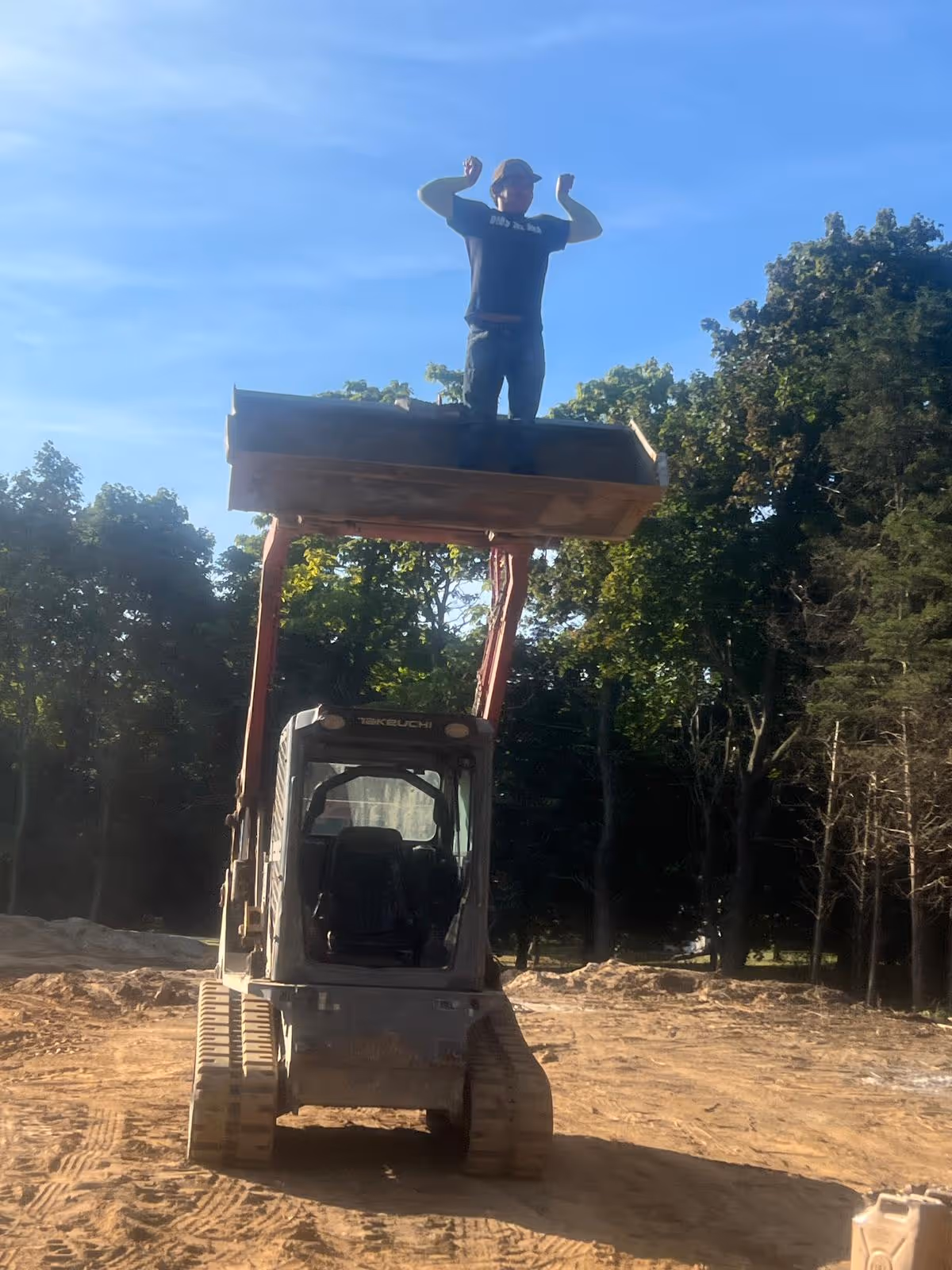 Man stands on a lifted platform atop an excavator at a construction site outdoors.