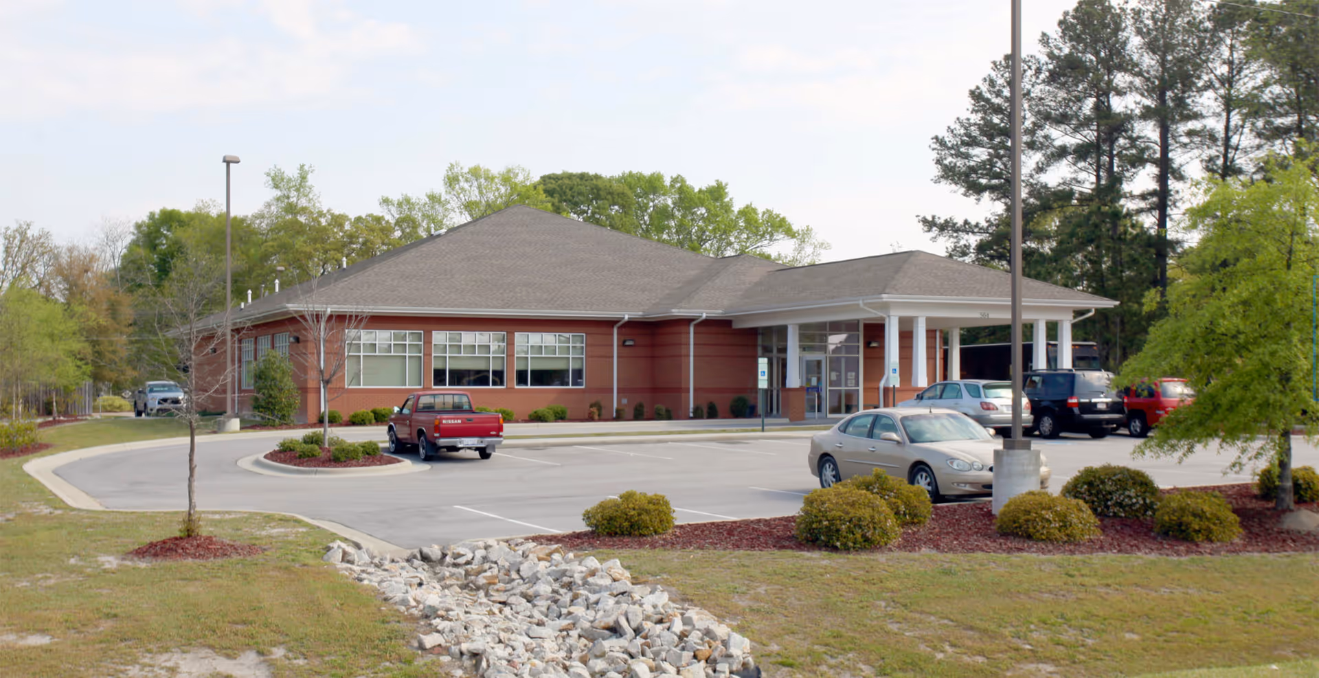 Brick single-story building with a covered entrance and a paved parking lot.