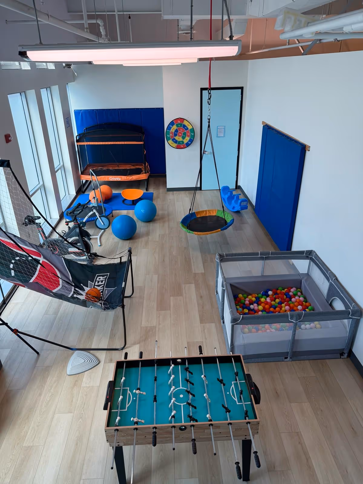 Indoor therapy playroom with foosball table, ball pit, swing, and exercise equipment.