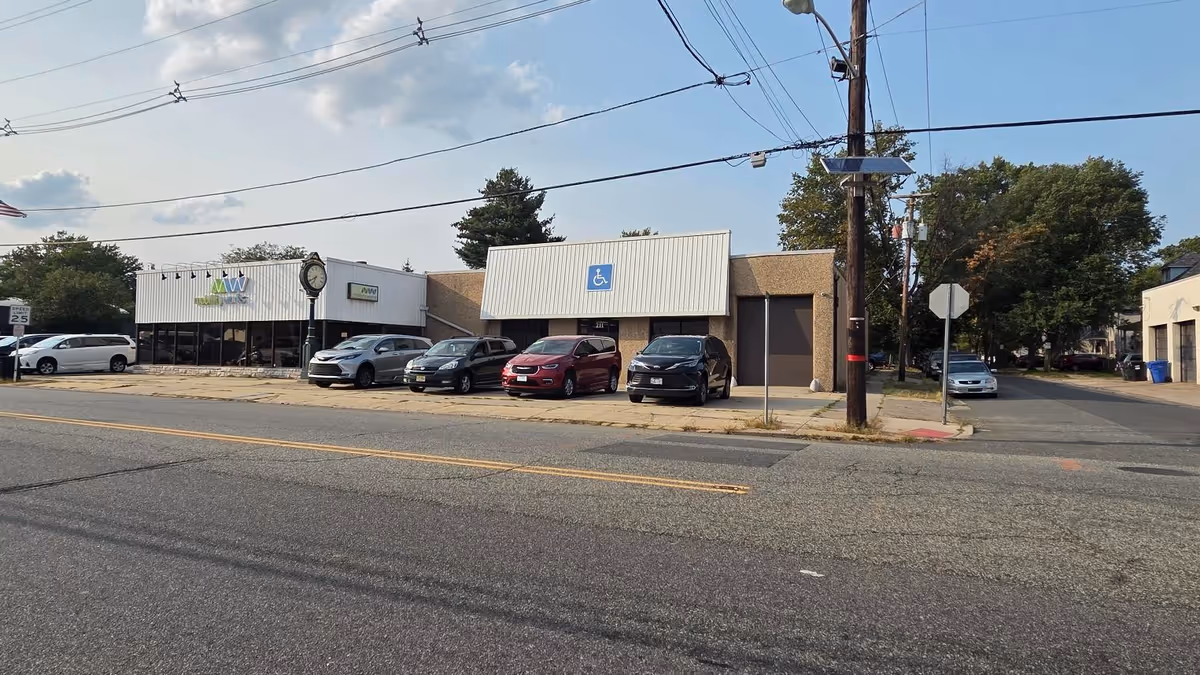 Street view of a row of storefronts with parked cars and a blue handicapped sign