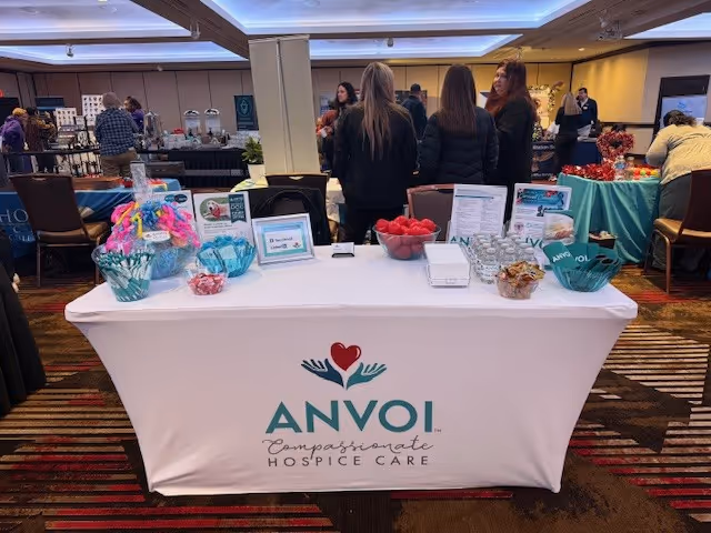 Indoor event with an Anvoi Hospice Care table and people mingling in the background.