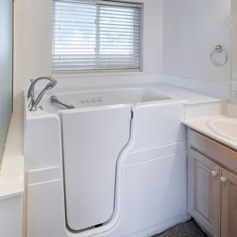 White walk-in bathtub with window, vanity, and towel ring in a bathroom.