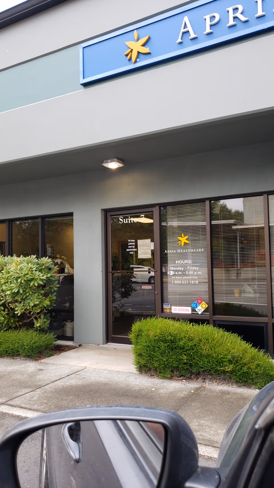 Exterior view of Apria Healthcare building entrance with glass doors and landscaping.