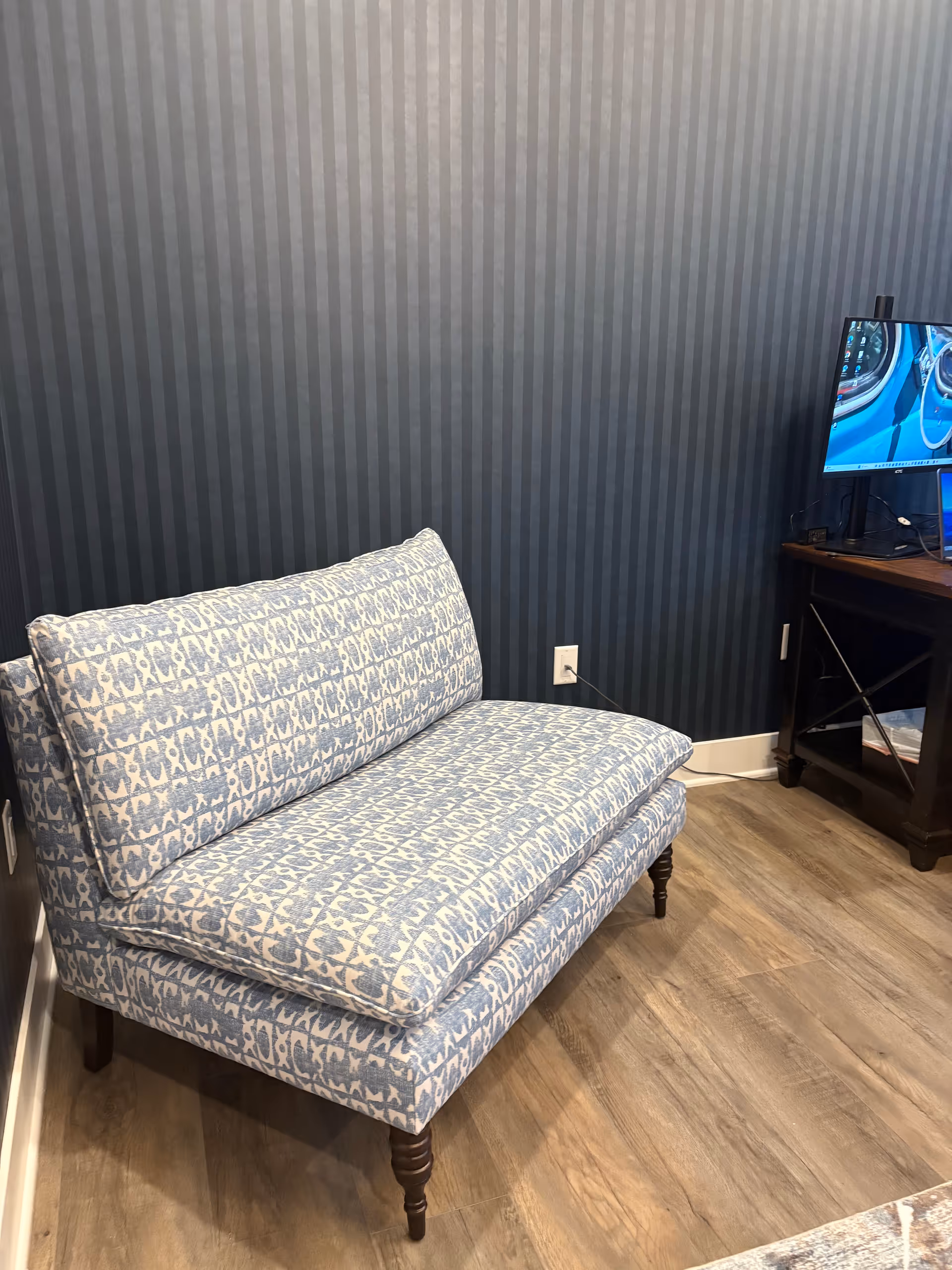 Blue striped wall behind a blue patterned sofa and a TV on a dark wooden stand.
