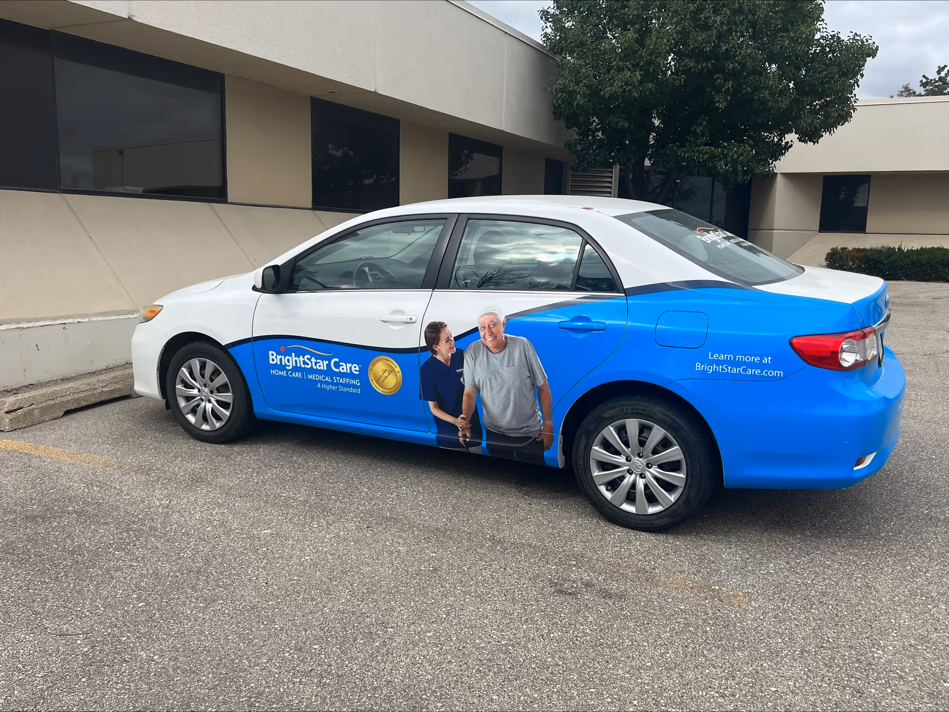 Blue and white BrightStar Care car parked outside a beige building.