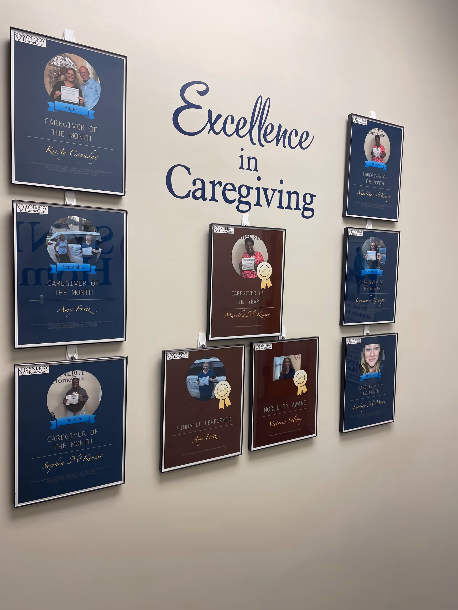 Wall inside a facility featuring framed Caregiver of the Month plaques and Excellence in Caregiving lettering.