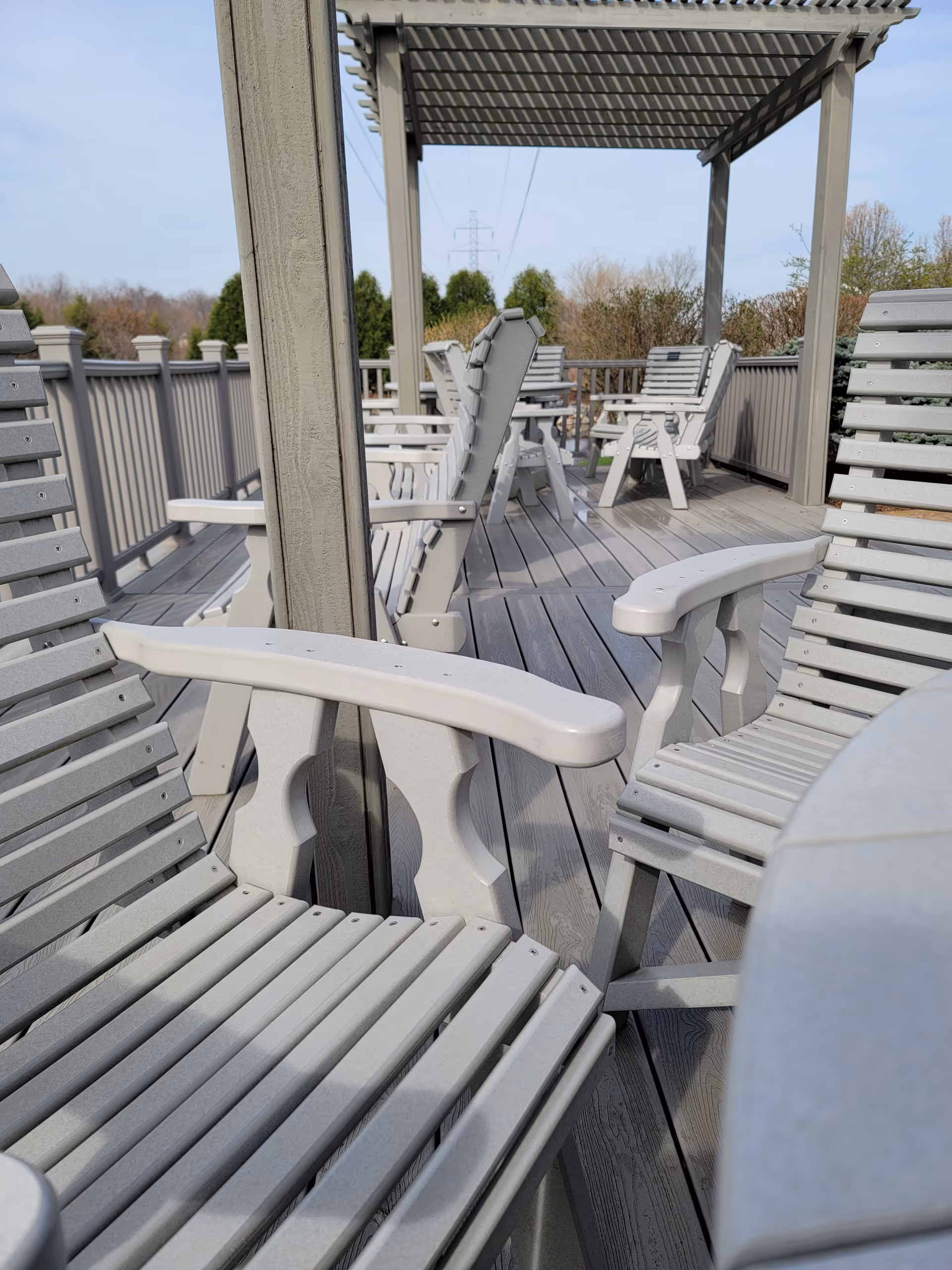 Outdoor deck with gray chairs arranged under a pergola.