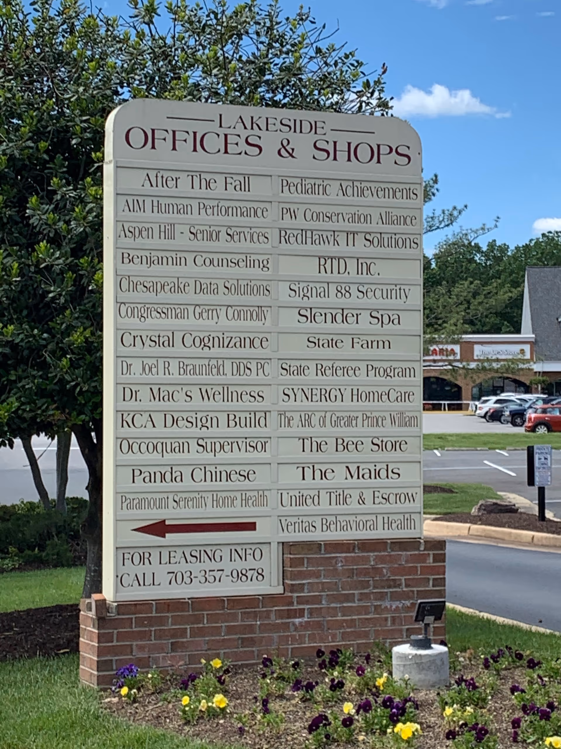 Large outdoor sign listing offices and shops, including SYNERGY HomeCare, near a parking lot.