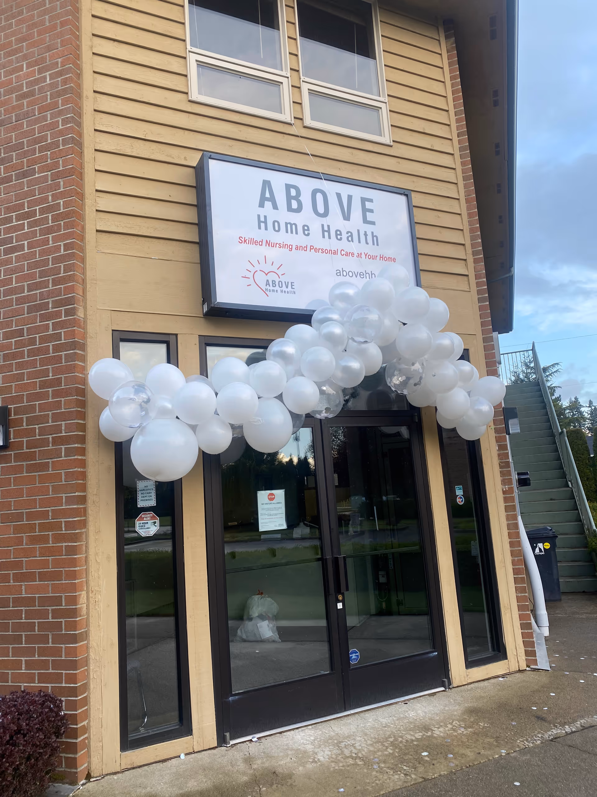 Exterior of ABOVE Home Health entrance with a white balloon arch above doors.