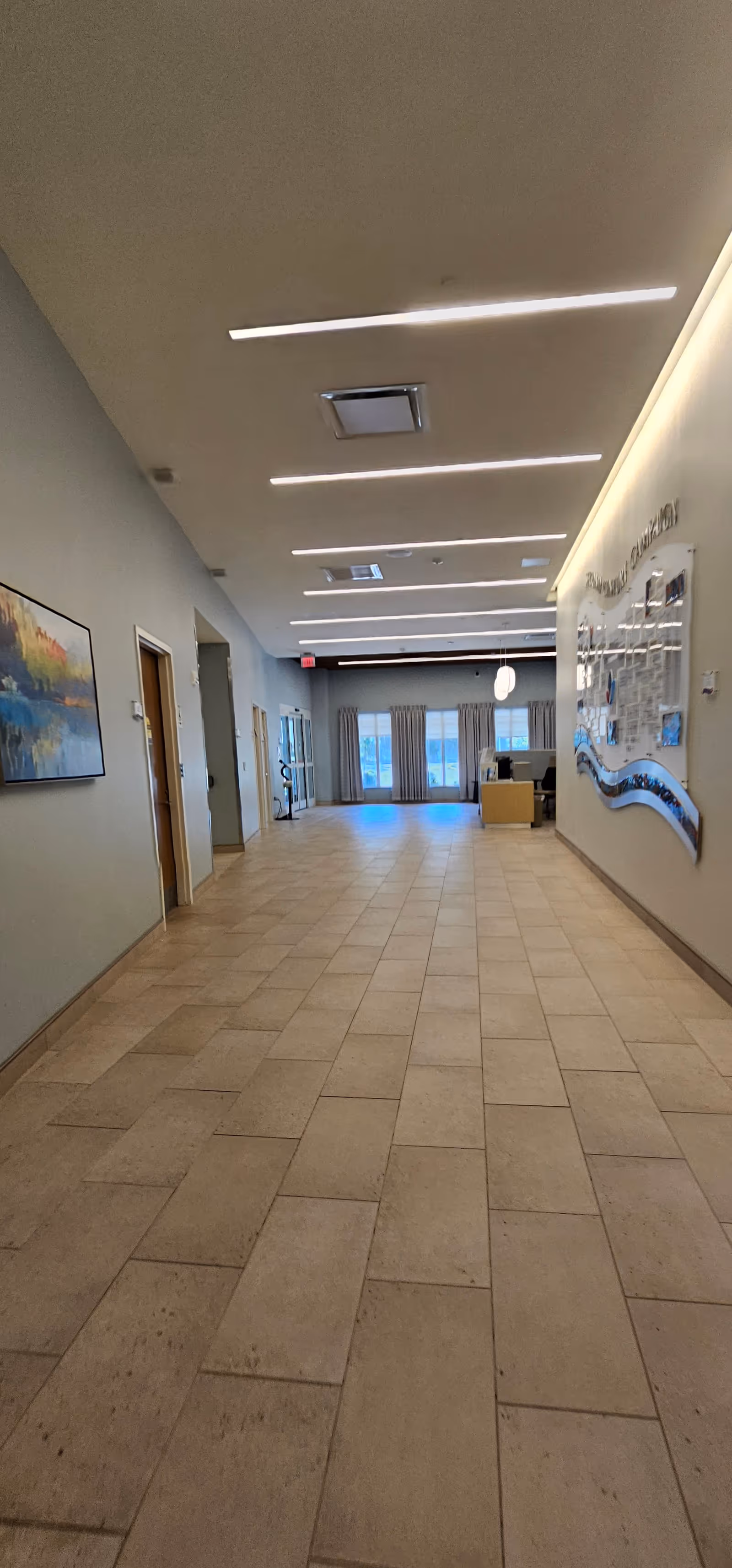 Long, well-lit interior hallway in a senior living facility with tiled floor and artwork.