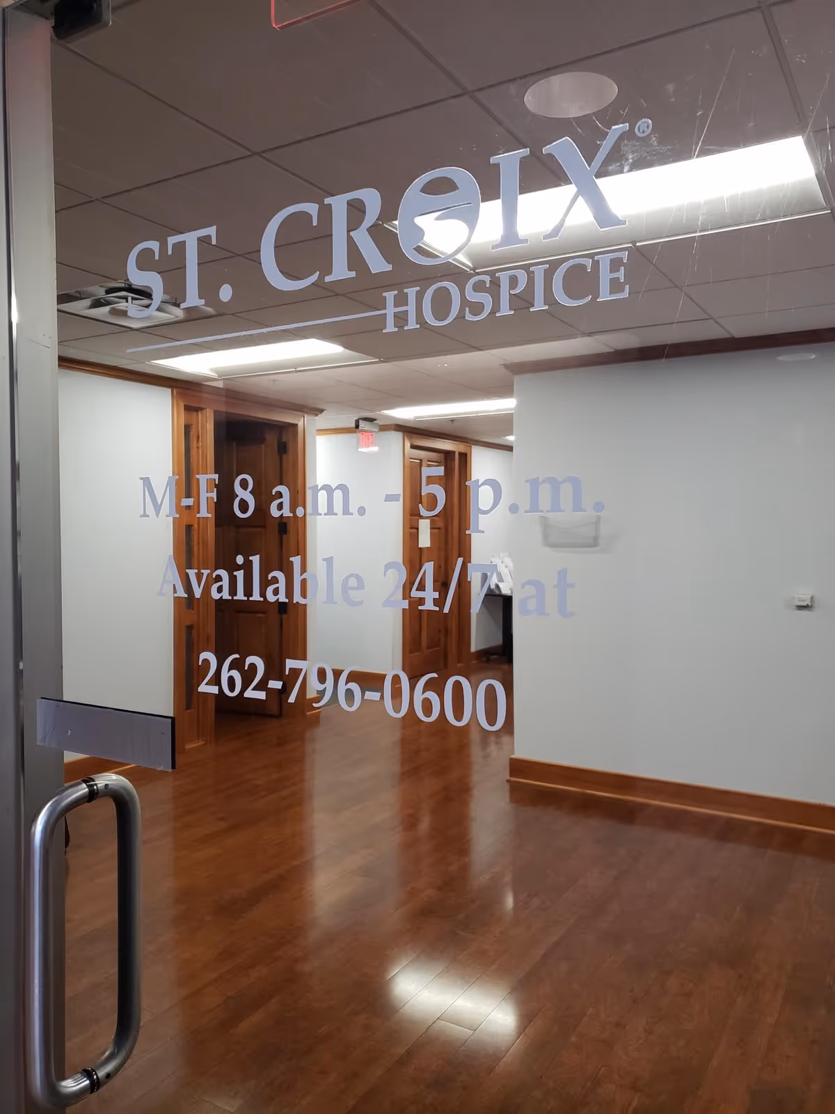 Glass door with St. Croix Hospice sign opens into a wood-floored interior hallway.
