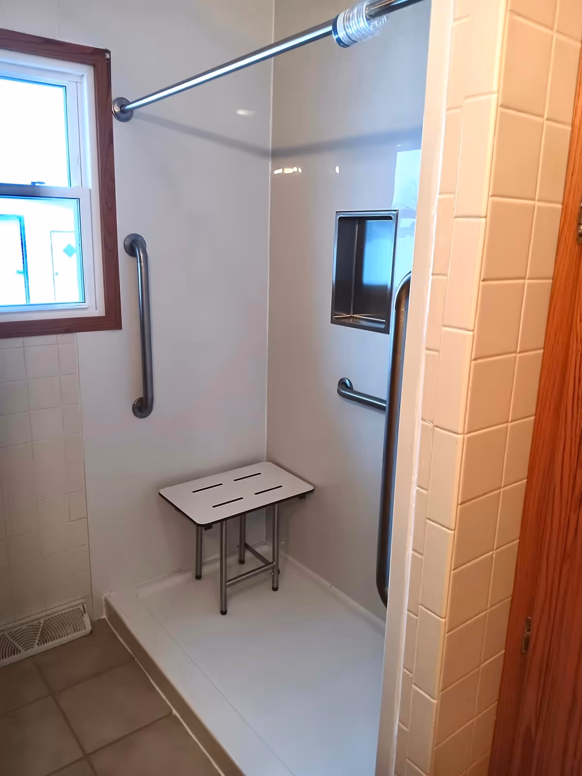 Accessible bathroom shower with a metal seat, grab bars, and tiled walls.