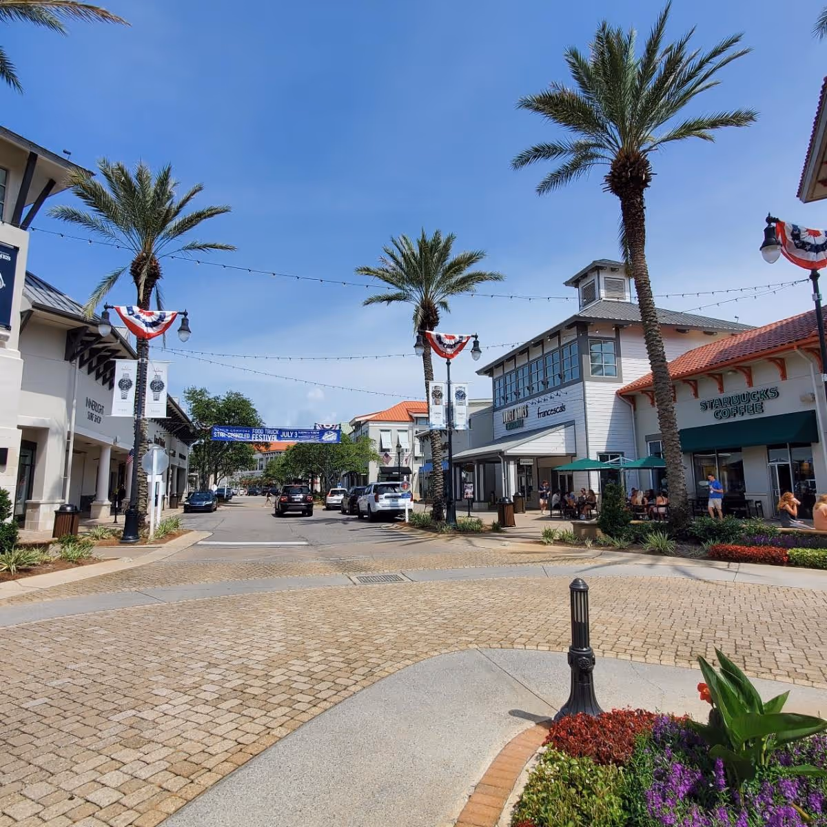 Sunny outdoor shopping district in Fort Walton Beach with palm trees and seating.