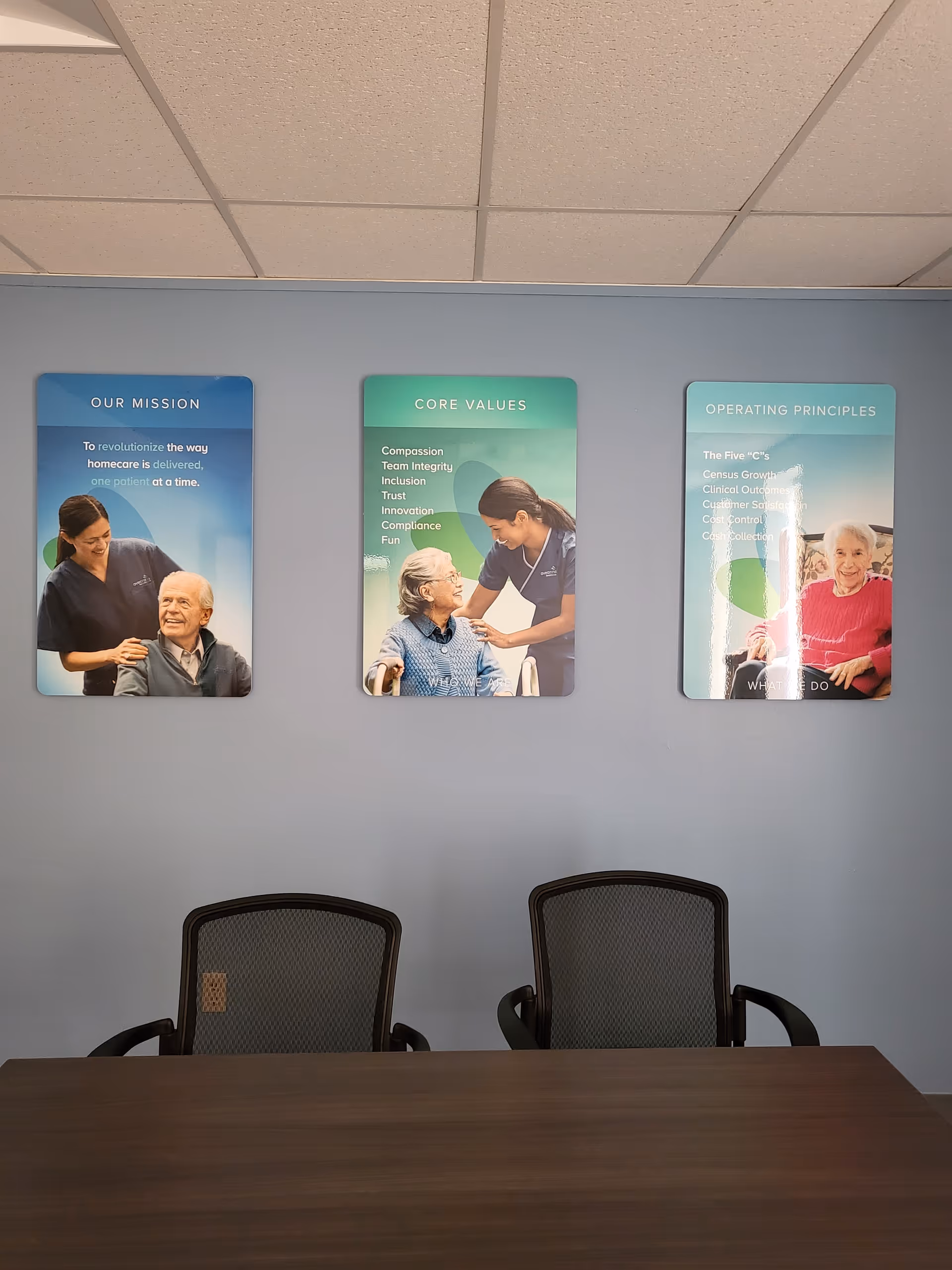 Interior meeting room with a wooden table, two chairs, and three posters on the wall.