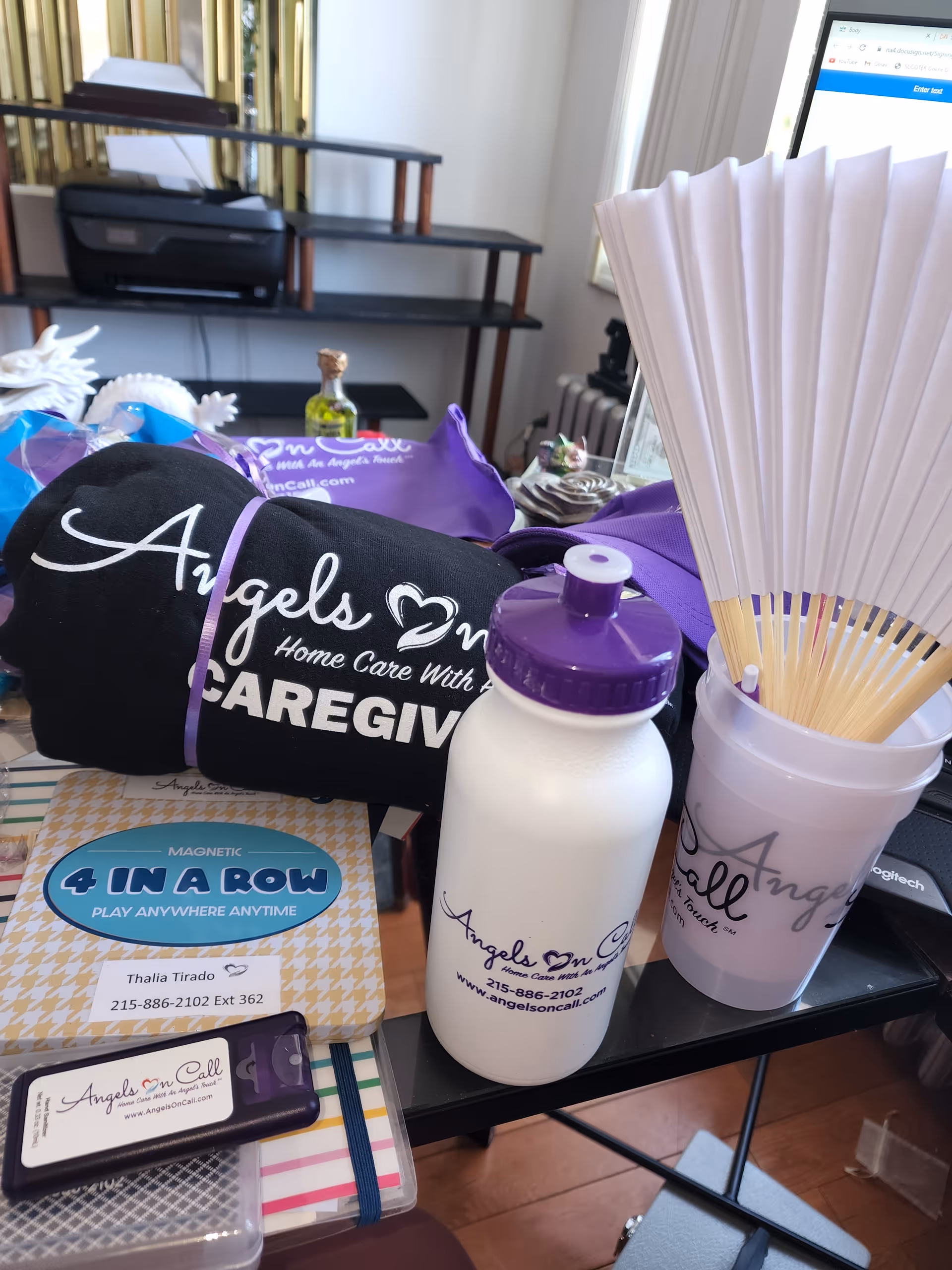 An office desk cluttered with Angels On Call Home Care branding items.