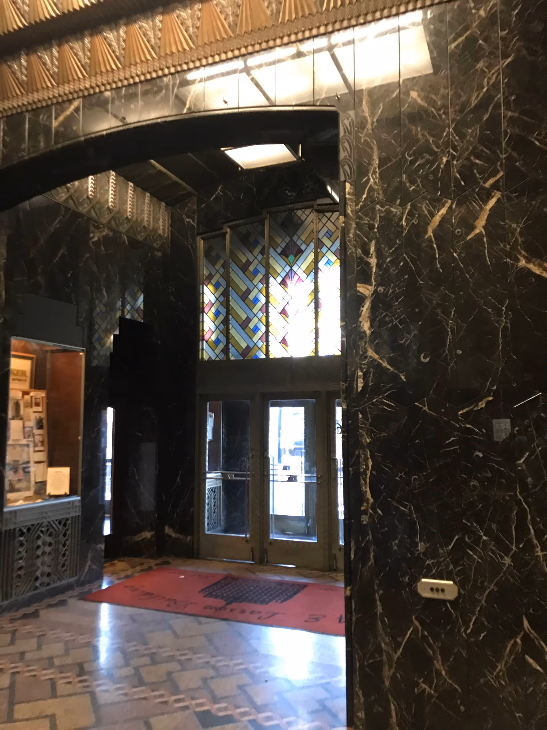 Grand marble lobby with archway, stained glass window, and double doors at the entrance.