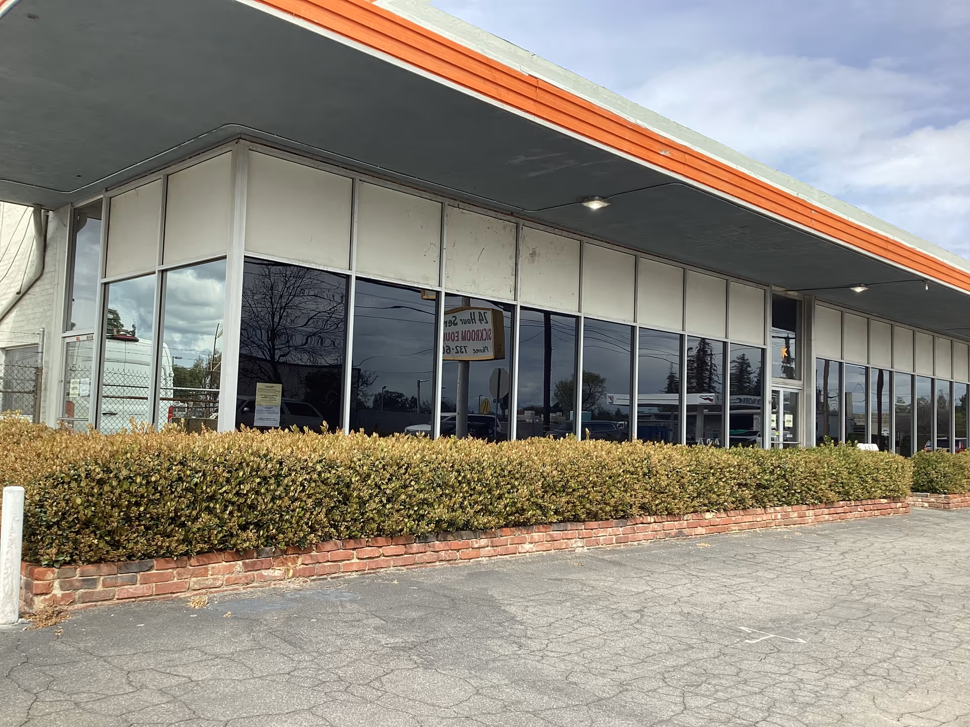 Glass storefront with large windows, orange trim, and a low brick planter along the parking lot.