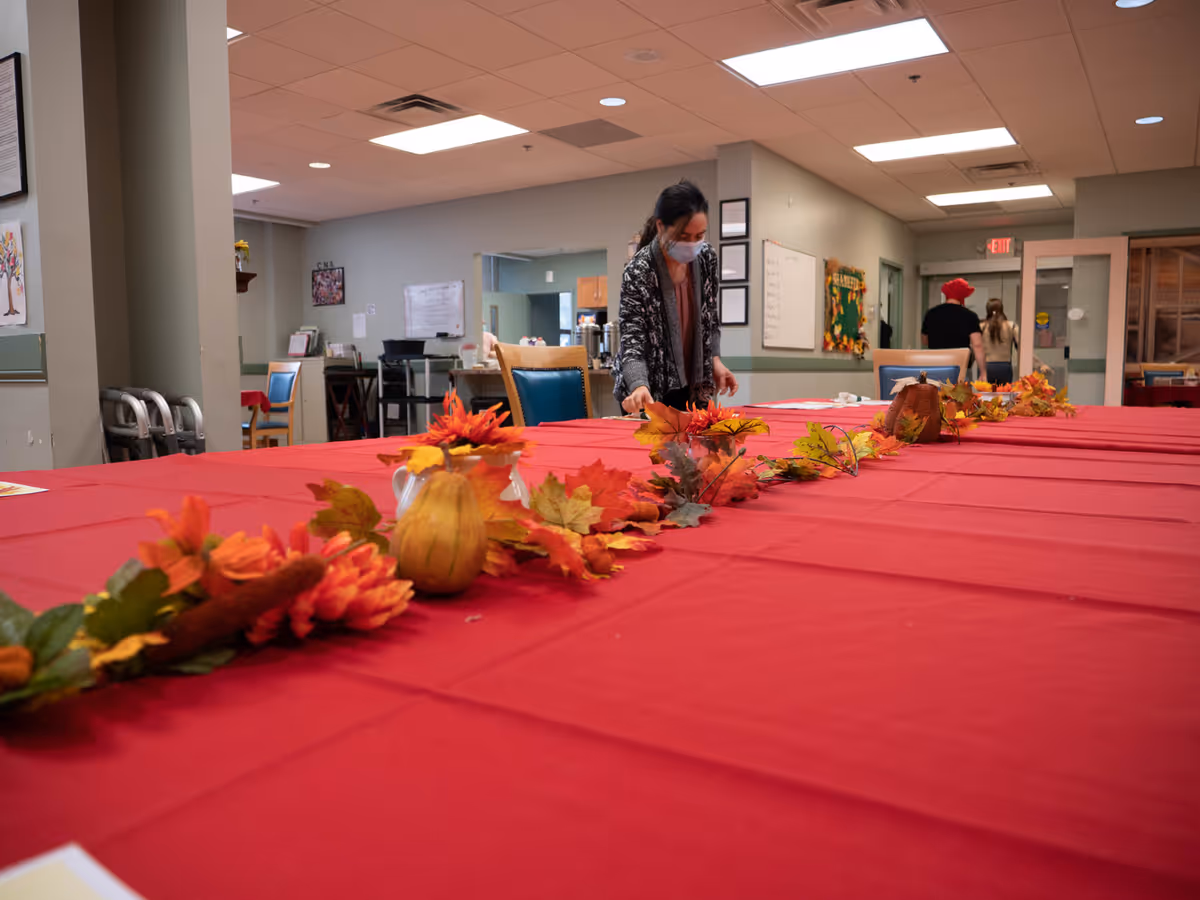 A long dining table with red tablecloth and autumn leaf centerpiece inside a senior facility.