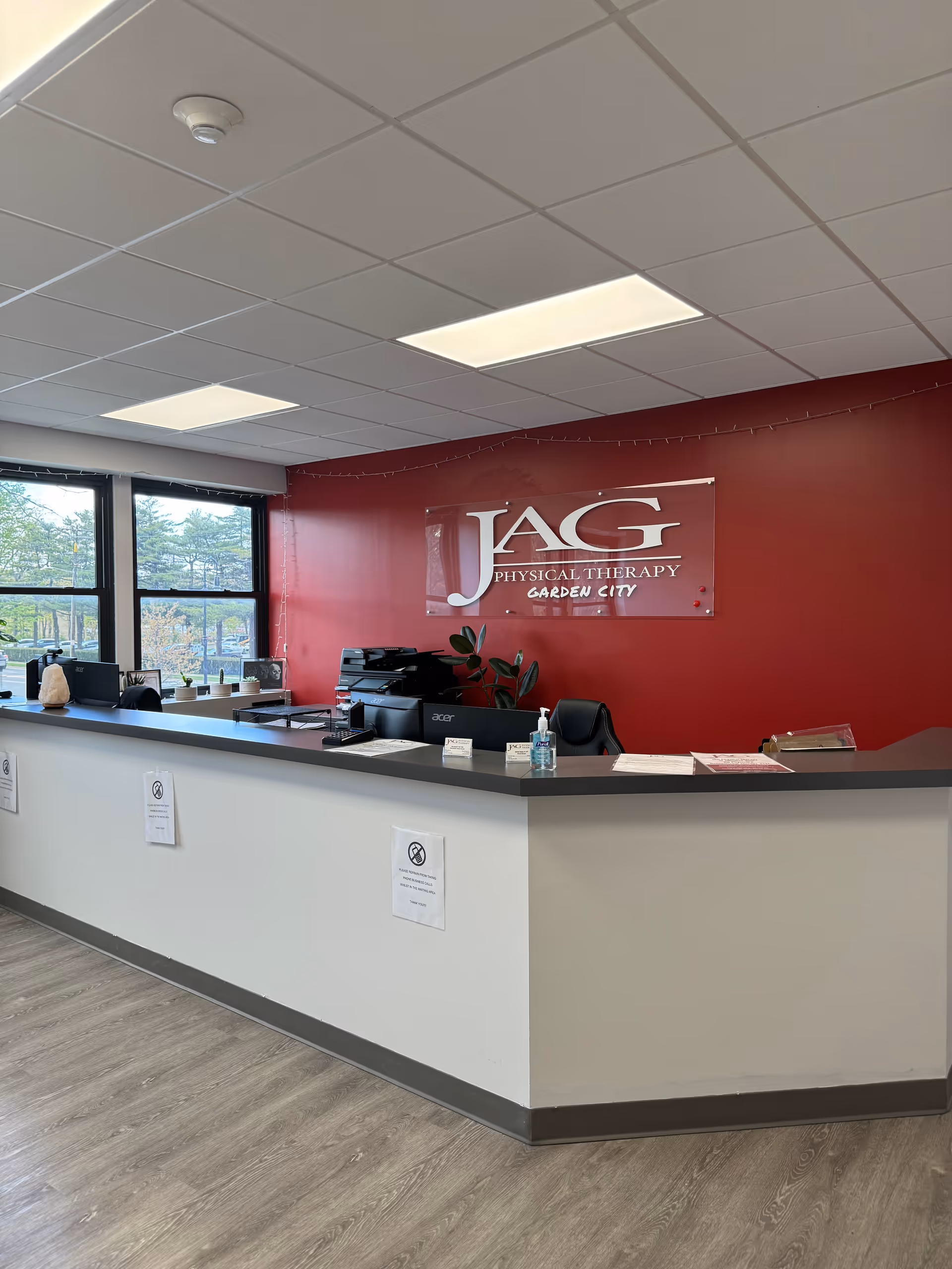 Interior reception area with a curved white counter, red wall sign, and large windows.