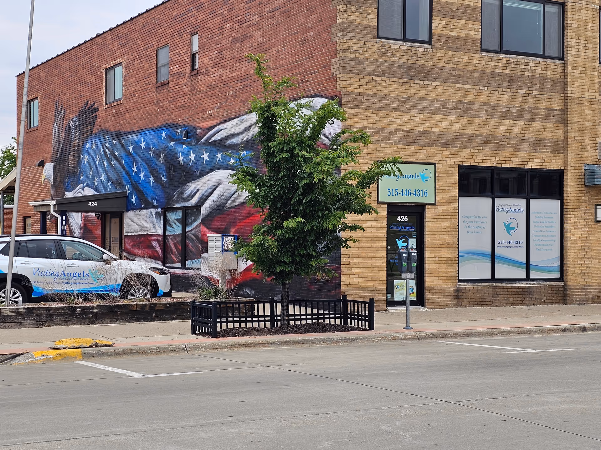 Brick building with large American flag mural, Visiting Angels storefront, and a parked company vehicle.
