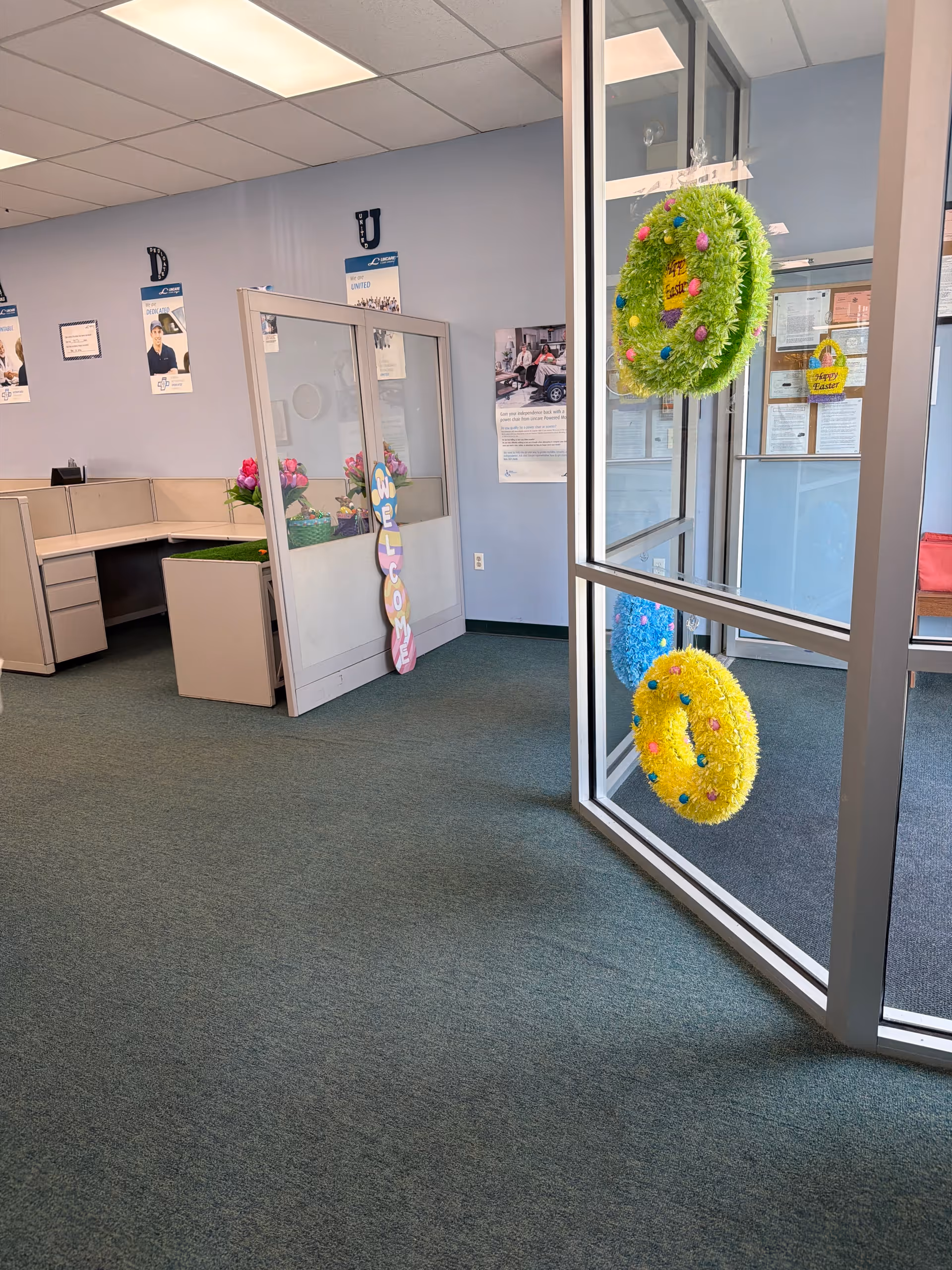 Interior of a senior living facility with cubicles, glass doors, and decorative wreaths.