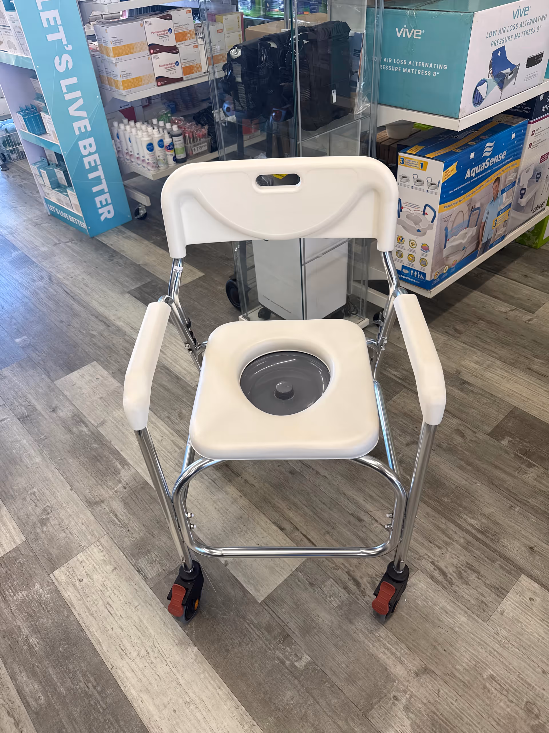 White wheeled commode chair displayed in a medical supply store showroom with boxed equipment