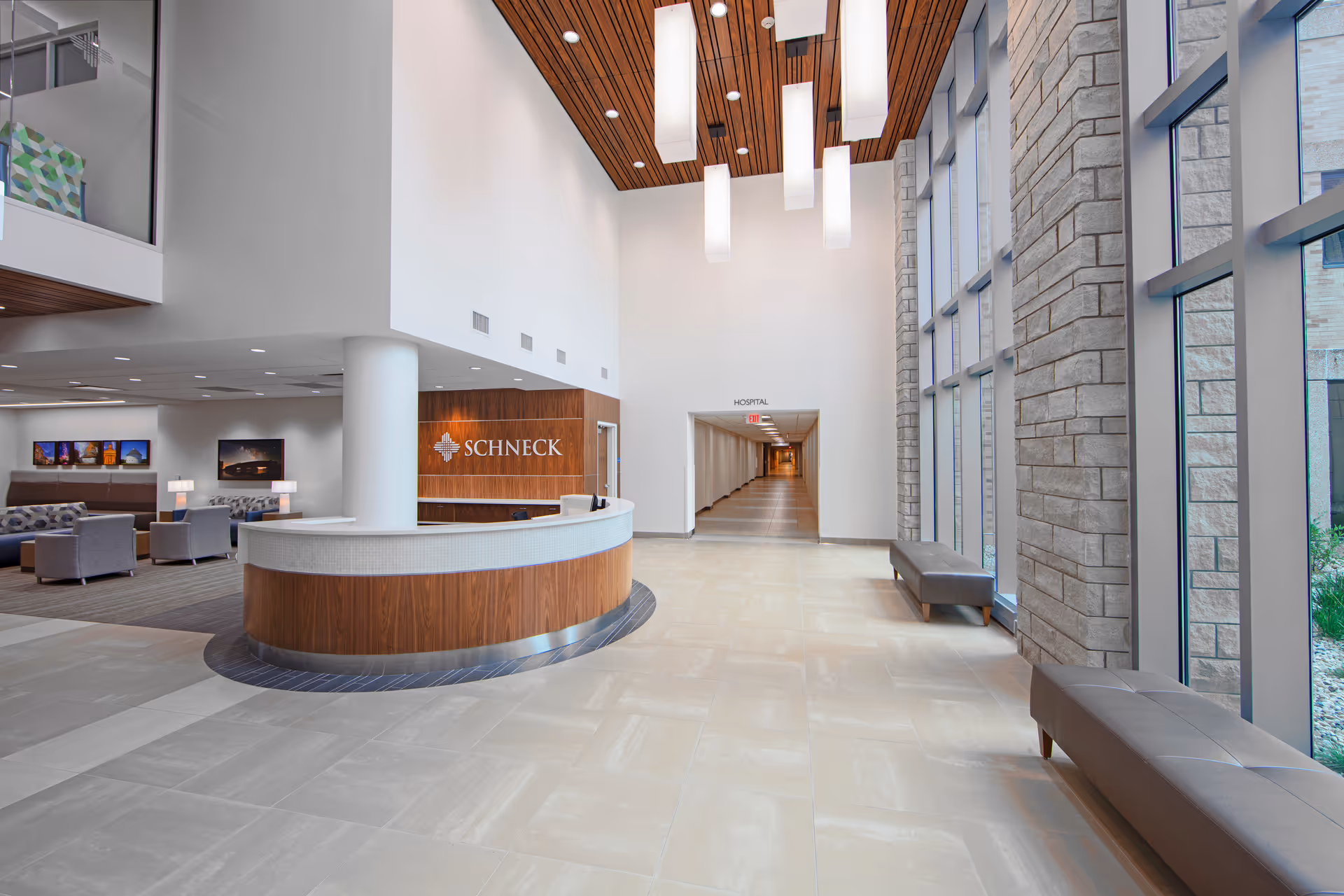 Modern hospital lobby with curved wood reception desk and ample seating by large windows