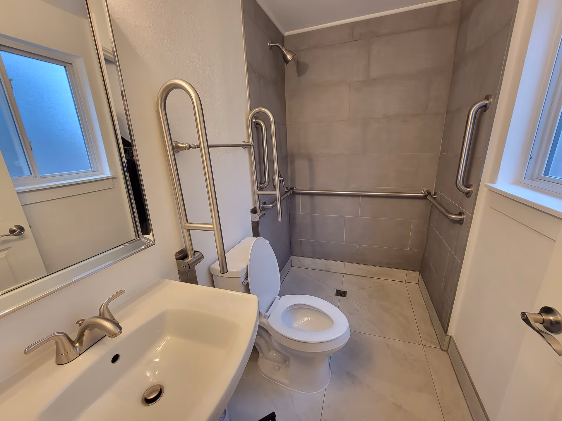 Accessible bathroom with grab bars, a toilet, sink, and tiled shower.