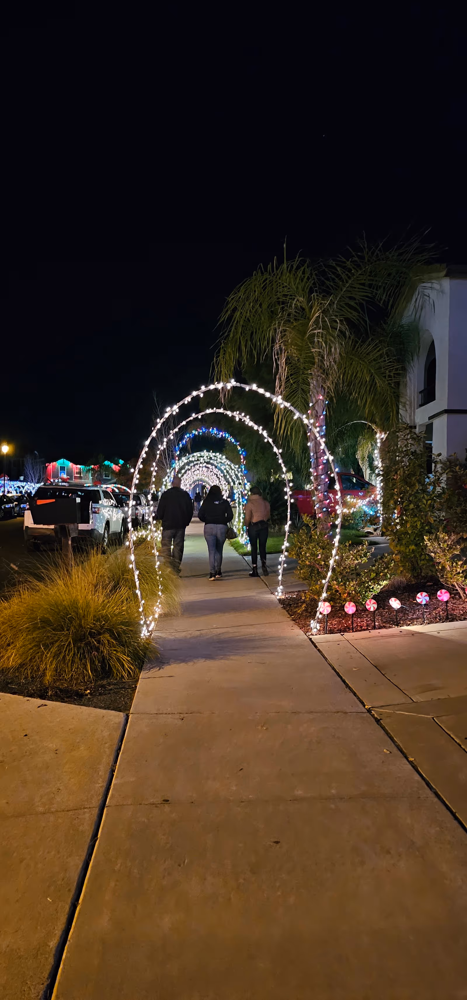 Nighttime outdoor walkway at Angel Care Services of Northern California shows illuminated arches and people strolling.