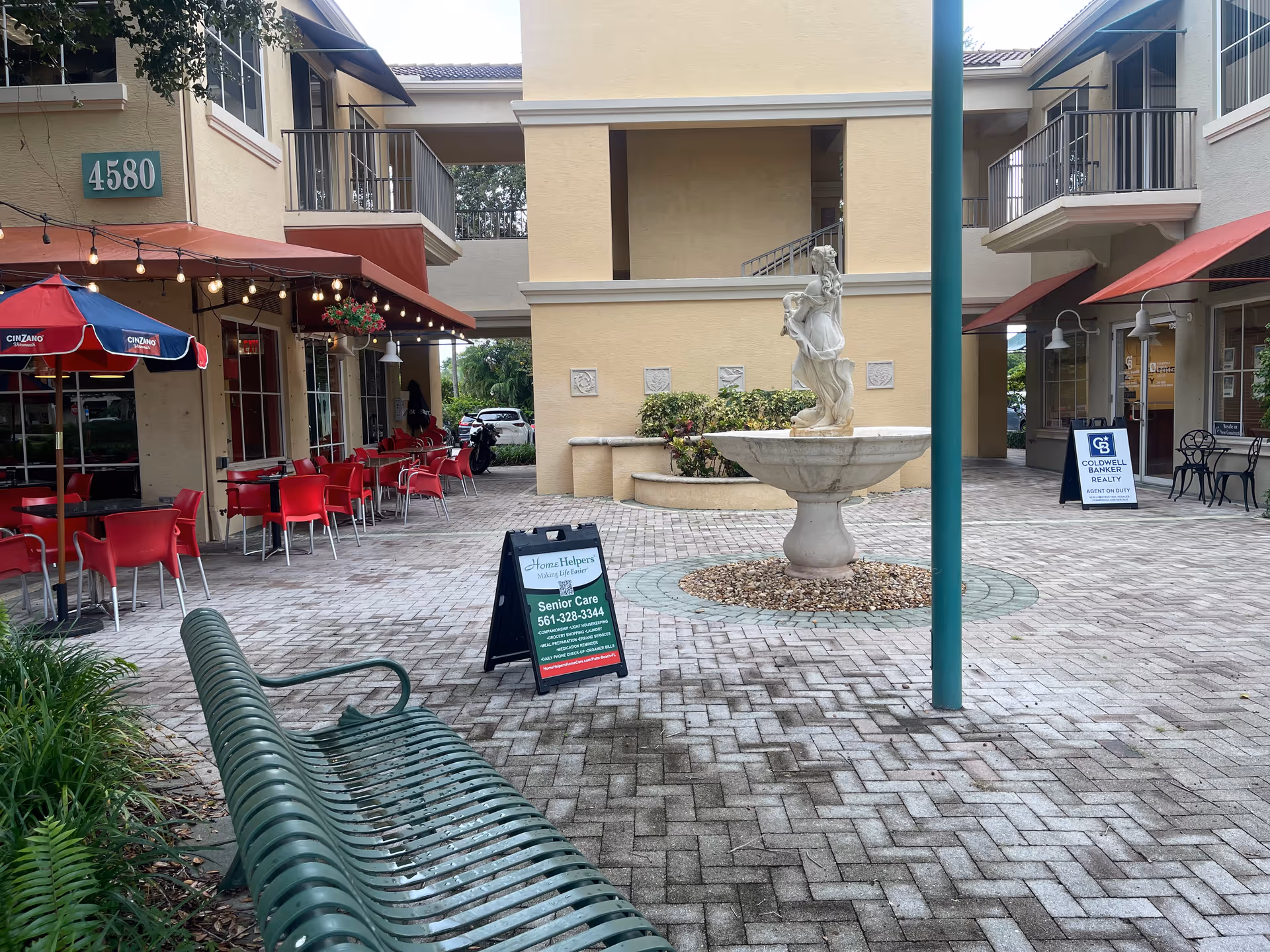 An outdoor courtyard with red seating, a central fountain statue, and building entrances.