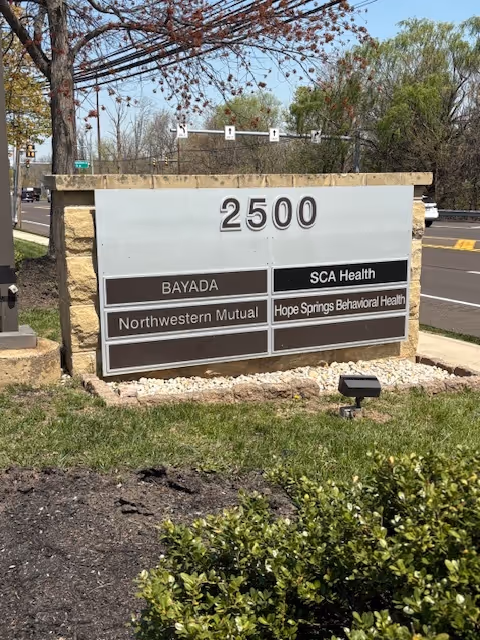 Outdoor facility sign displaying BAYADA and partner health services near a roadway