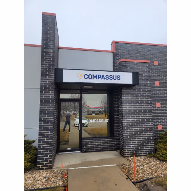 Brick facility entrance with Compassus sign and glass doors.