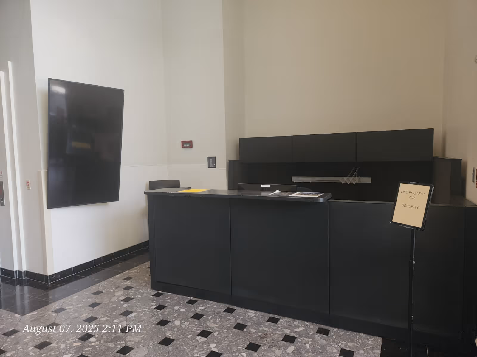 Dark reception desk in a modern interior lobby with a wall-mounted flat-screen TV.