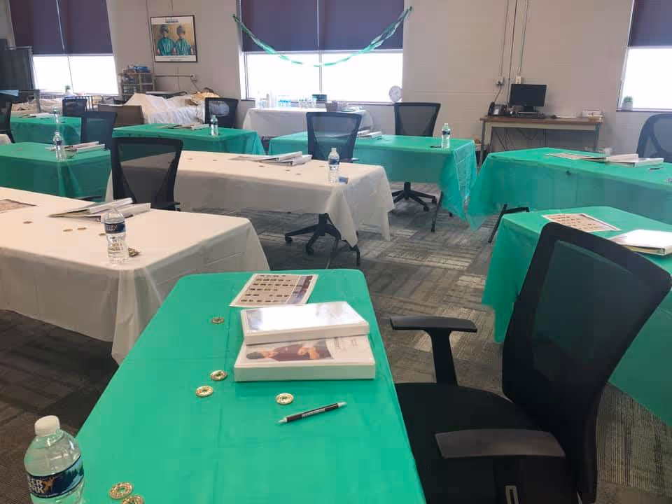 Empty conference room with green and white covered tables, chairs, and bottled water.