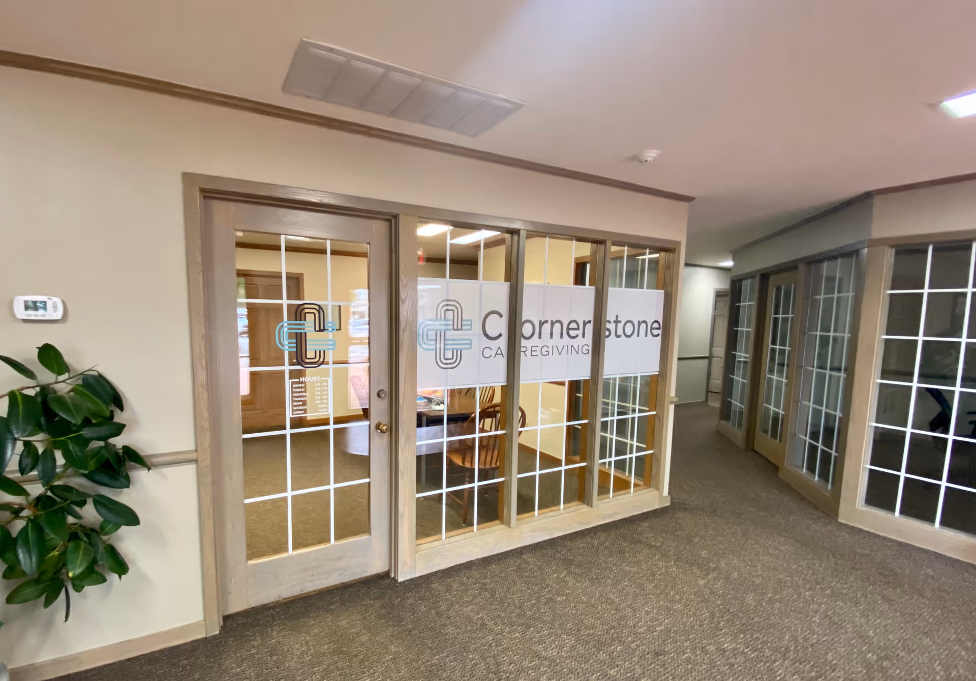 Interior hallway featuring glass doors with Cornerstone Caregiving signage and a potted plant.