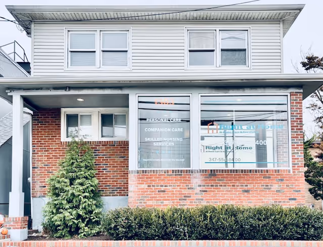 Two-story brick-and-siding building storefront with large windows and Right at Home sign, shrubs in front.