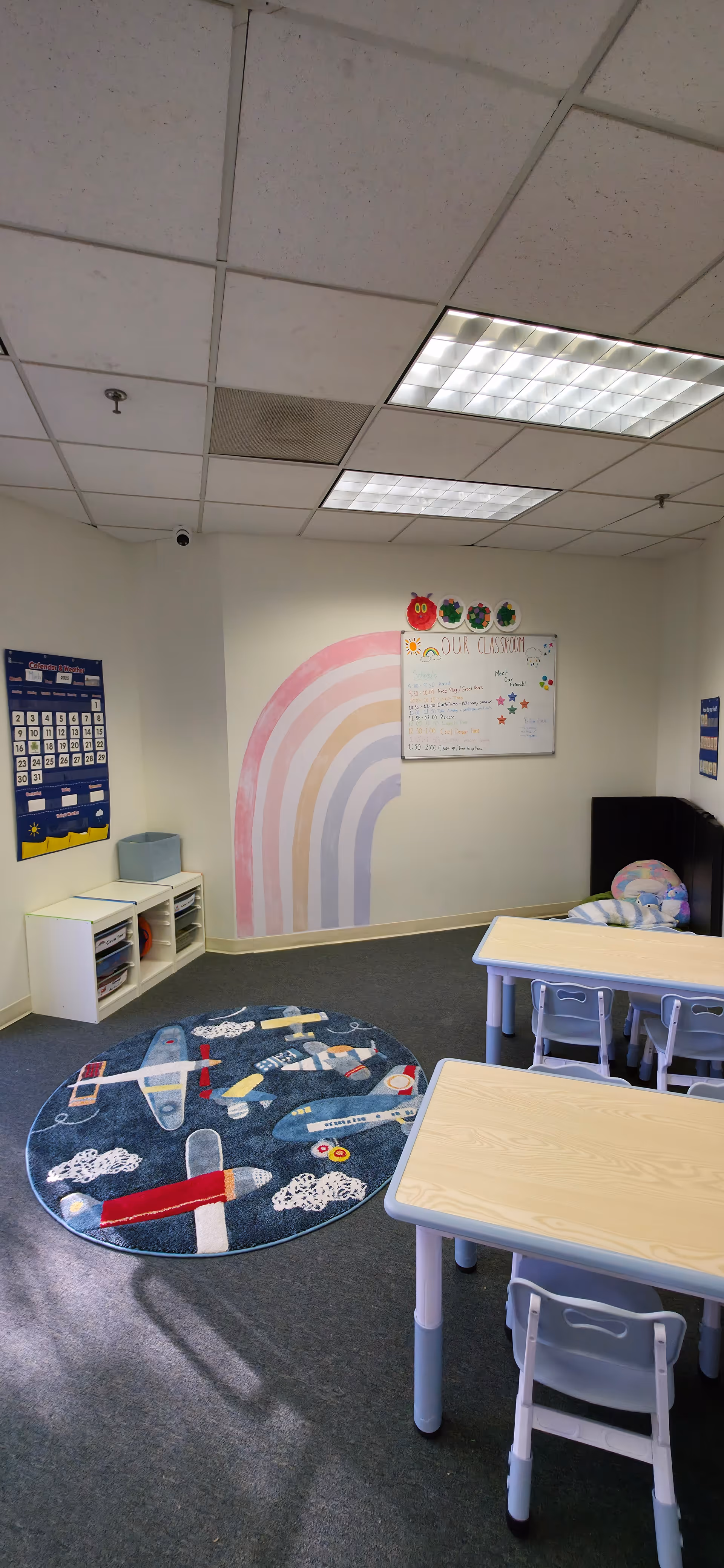 Interior children's therapy room with small tables, chairs, rainbow wall mural, and play rug.