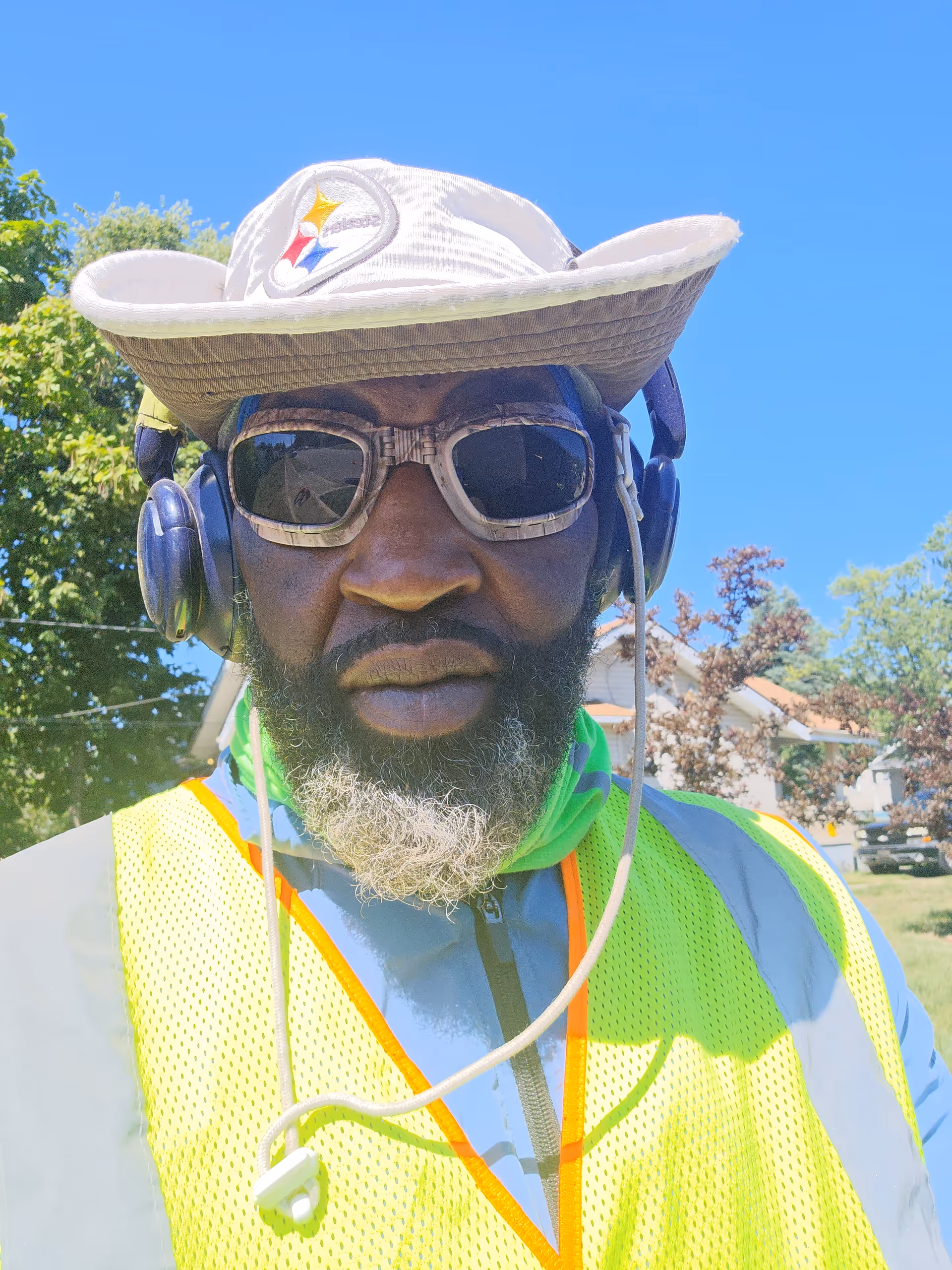 A worker wearing a high-visibility vest, hat, and sunglasses outdoors.