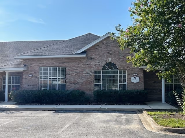 Brick building front of Amada Senior Care facility with arched window and landscaping.