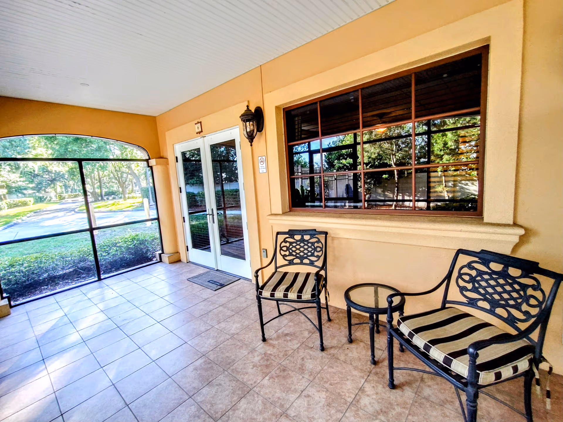 Covered outdoor seating area with striped chairs, a glass door, window, and tiled floor.
