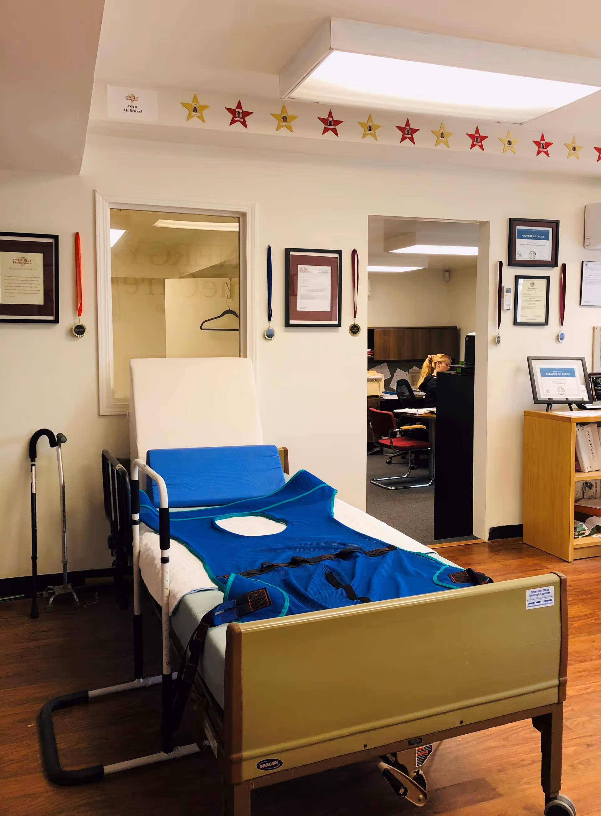 Hospital bed with blue linens in a senior care room; medals on the wall.
