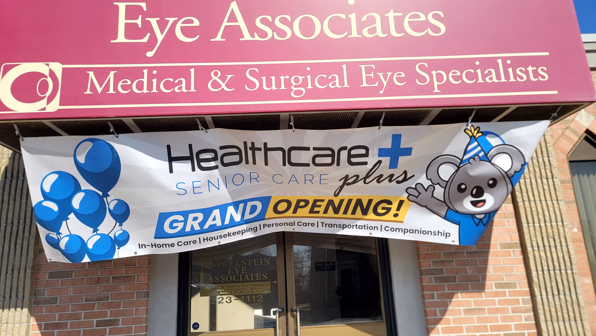 Exterior storefront with grand opening banners for Healthcare Plus Senior Care and Eye Associates.