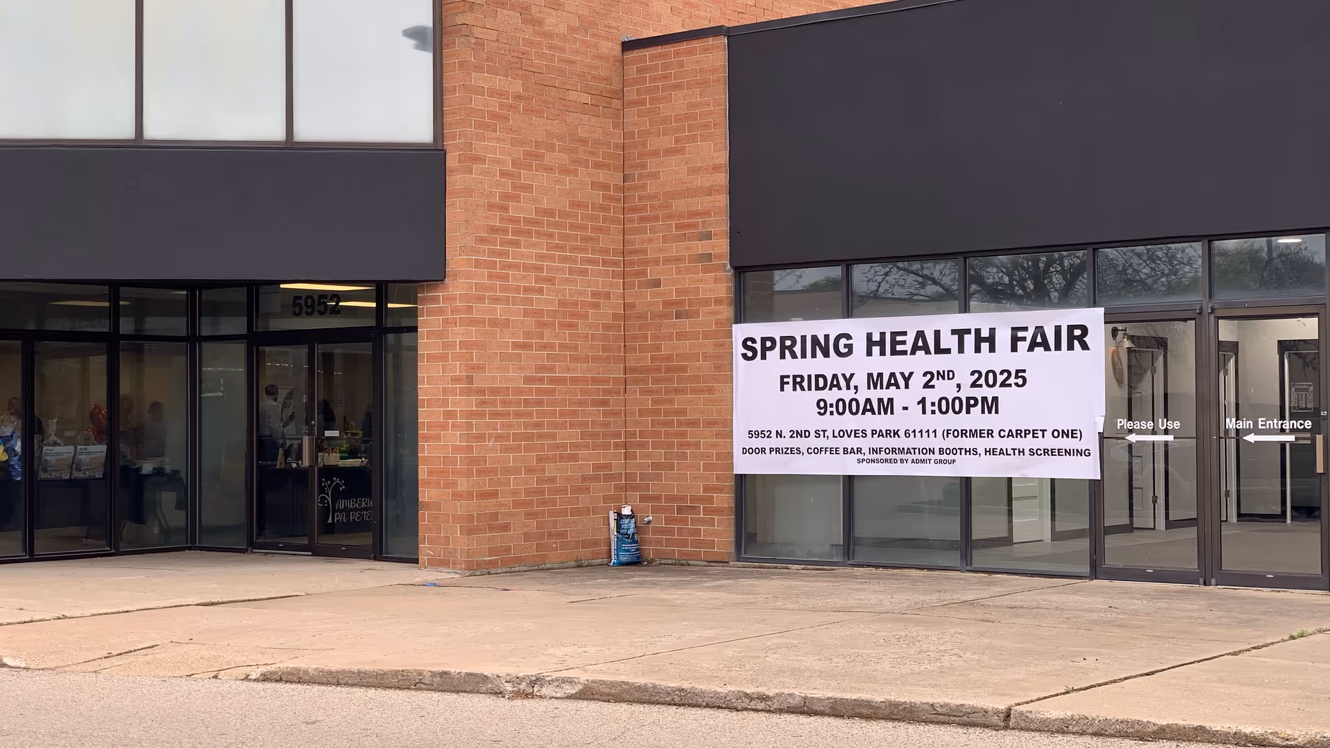 Brick storefront exterior with a large Spring Health Fair banner displayed outside