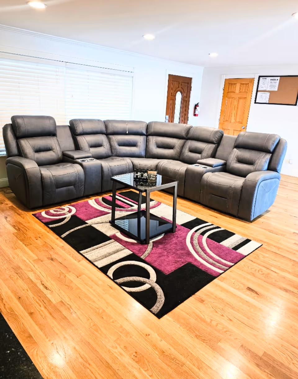 A large grey leather sectional sofa with a glass coffee table in a bright living room.