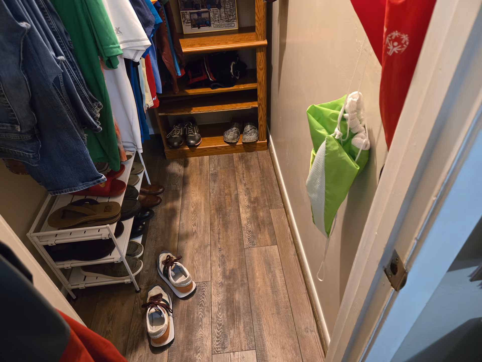 Narrow closet with coats, shelves, and multiple pairs of shoes on a wood floor