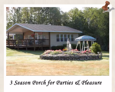 Cream colored building with a wooden porch, fountain, and circular flower bed in a lawn setting.