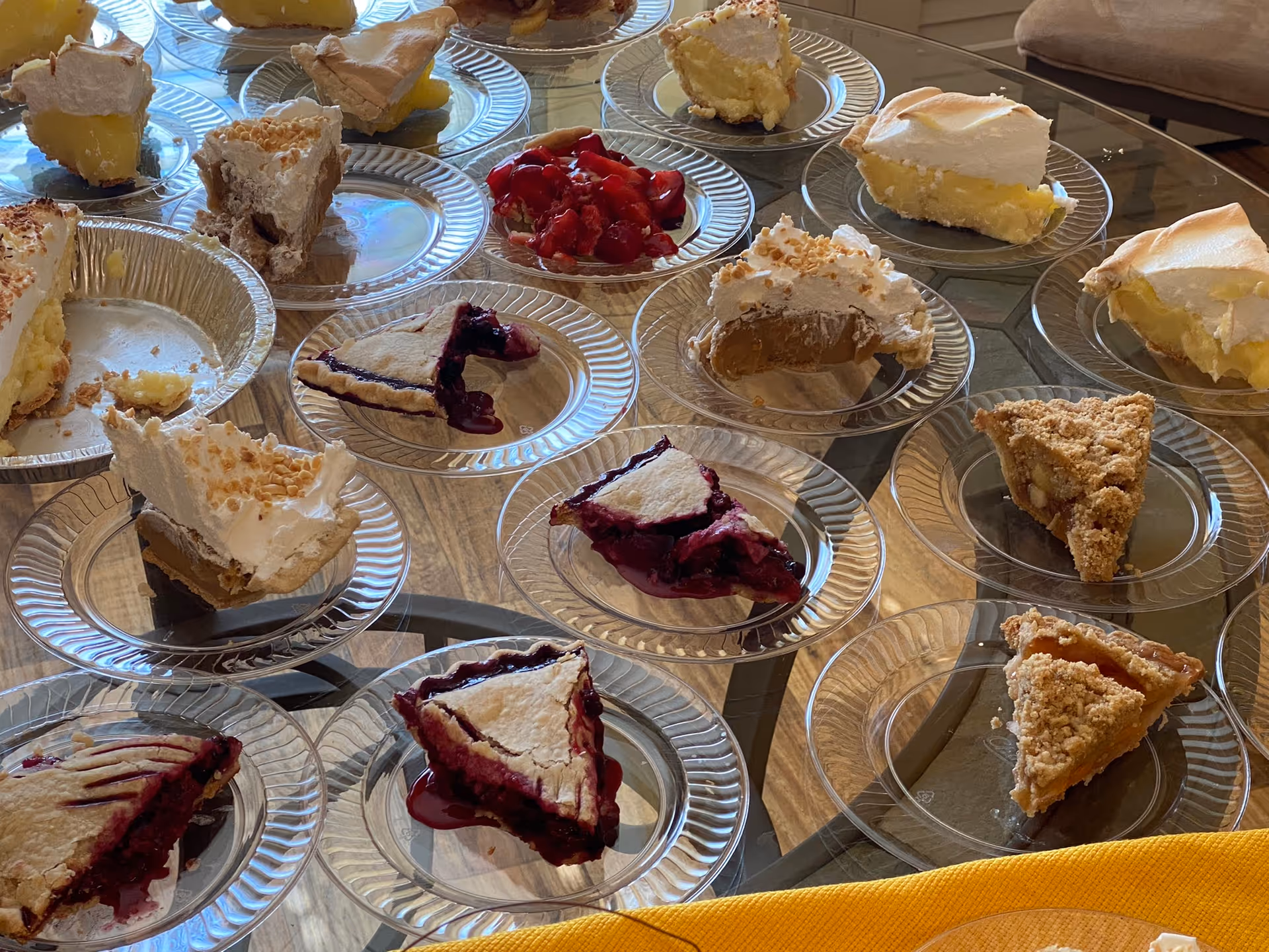 Assorted cake slices arranged on clear plates atop a glass dining table indoors.